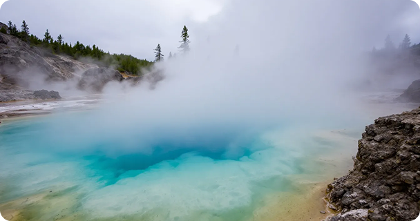 The image depicts the vibrant geothermal hot springs of Yellowstone National Park, with steam rising into the air, showcasing the thermal energy released from the earth. This natural phenomenon illustrates the transformation of geothermal energy into visible steam, highlighting the park's unique geological features.